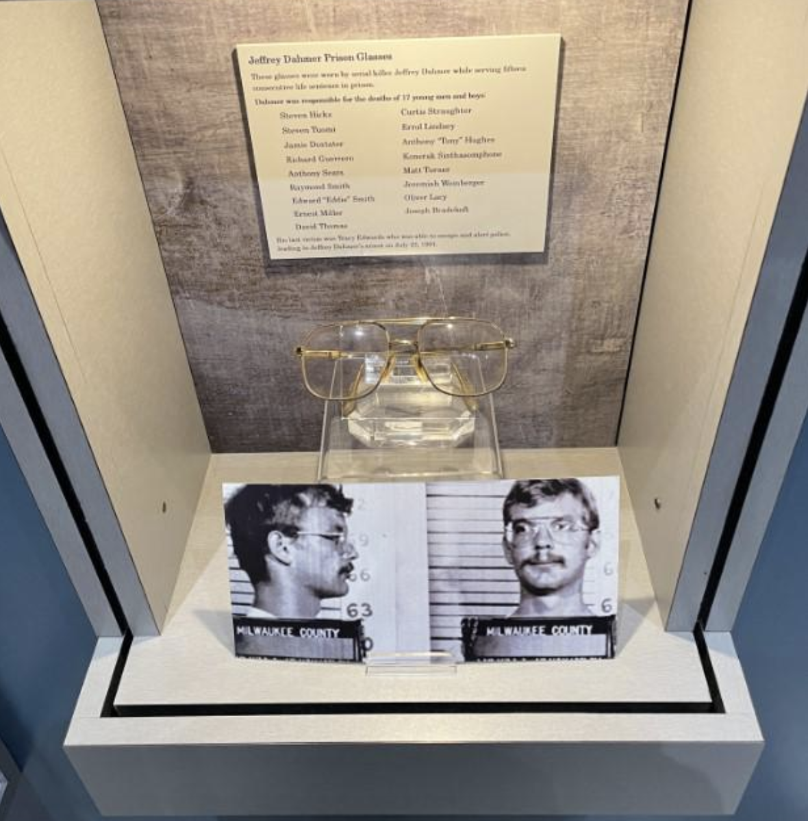 Display case with Jeffrey Dahmer's prison glasses and two mugshots. Text above describes the item's history and list of donation contributors