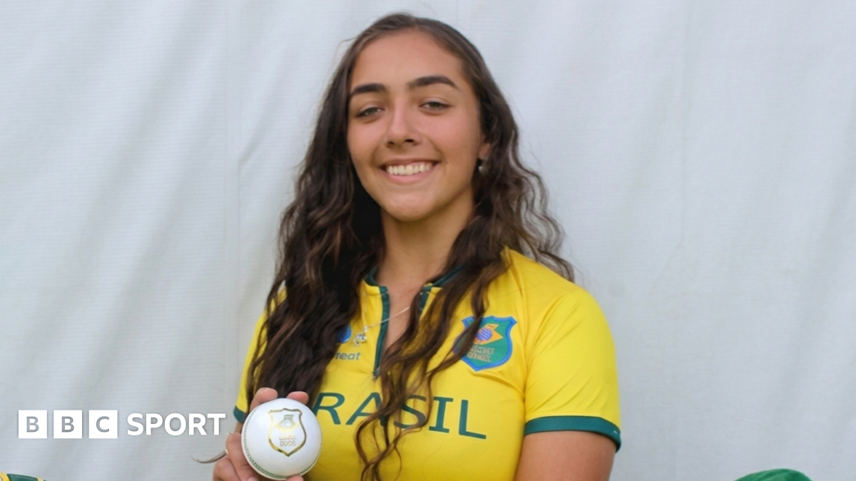 Laura Cardoso holding a white ball while wearing a Brazil cricket kit