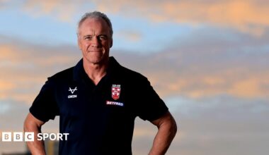 Brian McDermott, wearing a black England polo shirt, looks to the camera, with the sky in the background