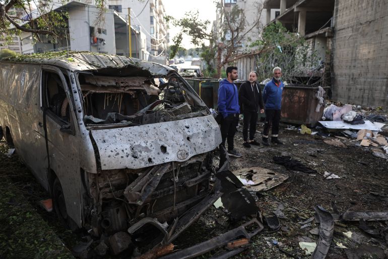 Men look at the damage next to the wreckage of a vehicle at the site of an Israeli strike in Beirut on April 1, 2026.