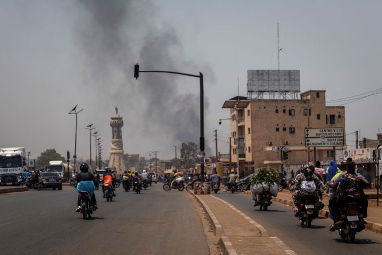 TOPSHOT - A column of black smoke rises above buildings as traffic passes the Africa Tower monument in Bamako on April 26, 2026.