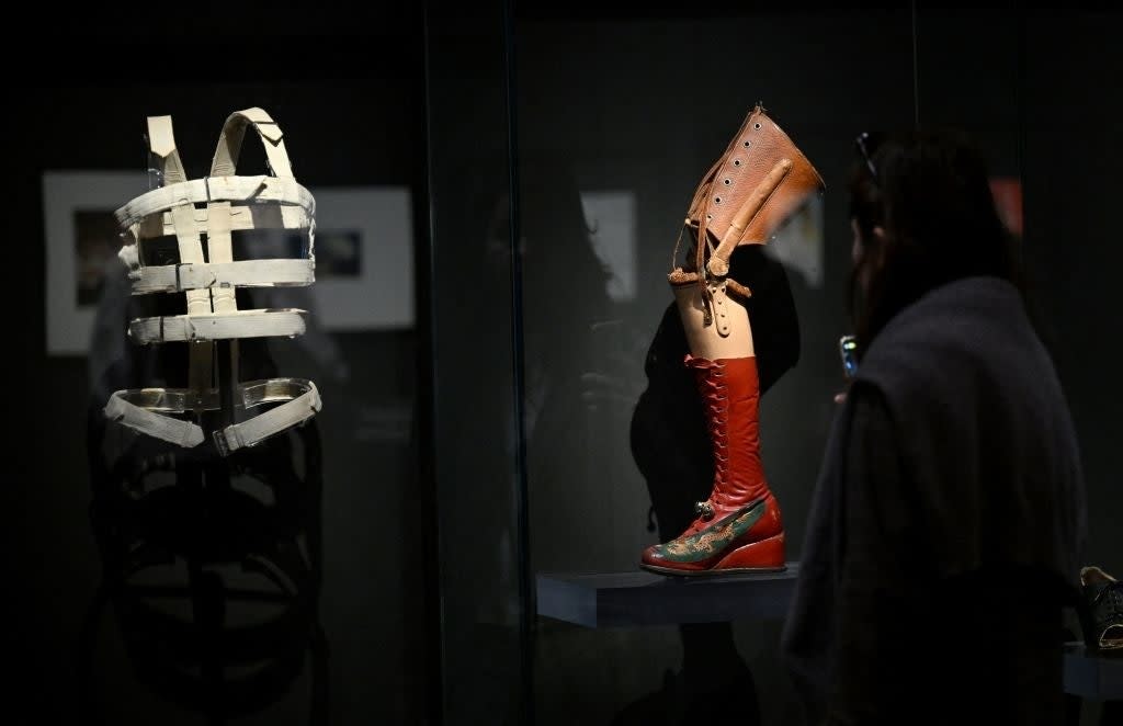 A person views historical orthopedic devices in a museum exhibit, including a leg brace and corset