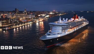 The Queen Mary 2 ocean liner on the River Mersey at night. The Liverpool waterfront and Liver Building is lit up in the background.