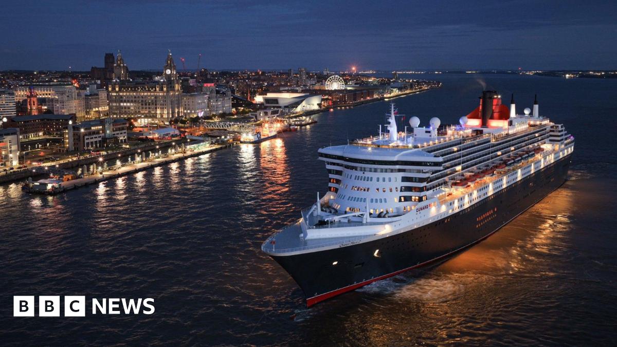The Queen Mary 2 ocean liner on the River Mersey at night. The Liverpool waterfront and Liver Building is lit up in the background.