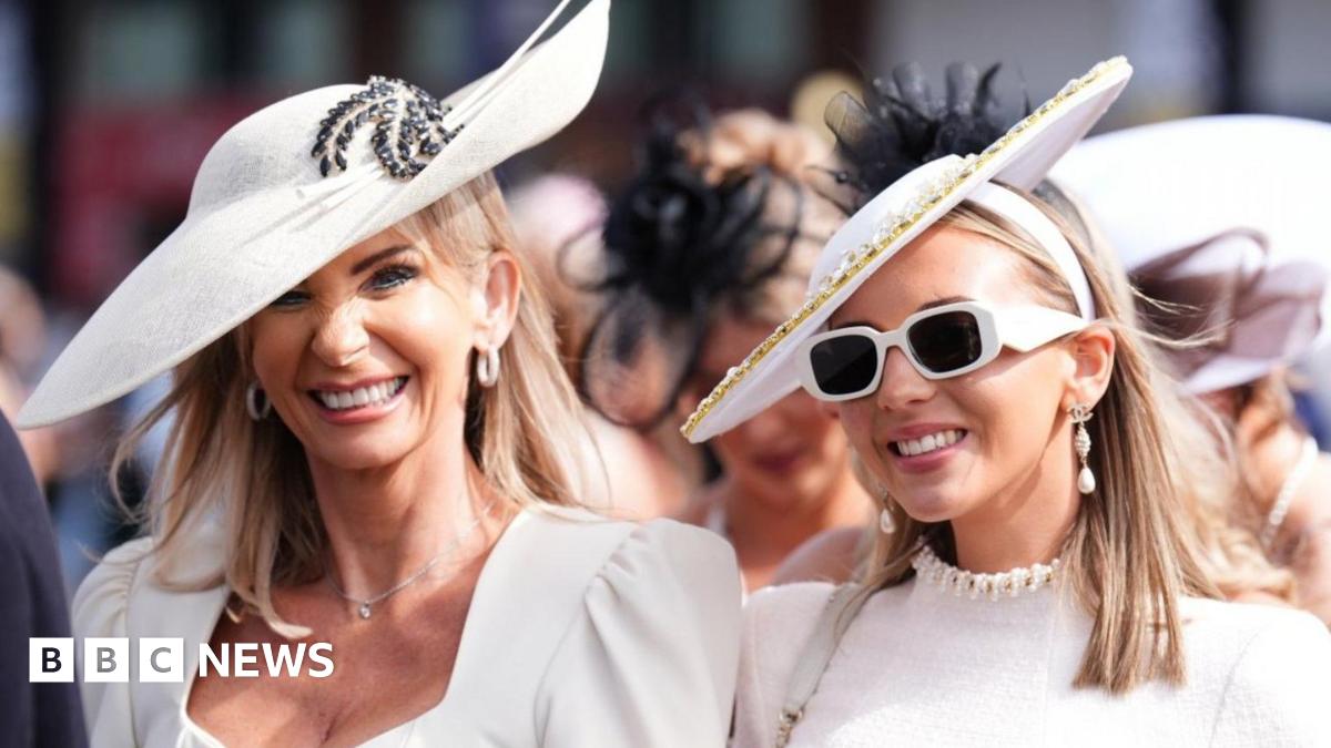 Two women wearing white dresses and hats arrive at Aintree