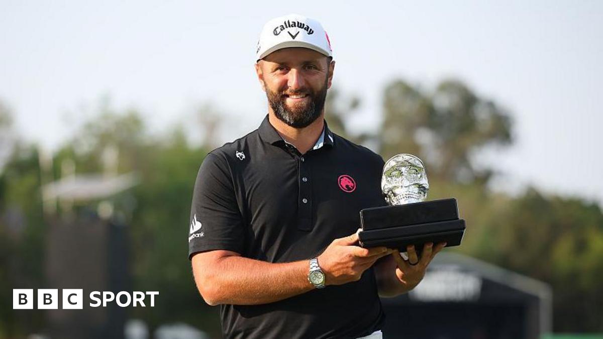 Jon Rahm, with a dark beard and wearing a black polo shirt, smiles as he holds the LIV Mexico trophy - a black base with a glass skull