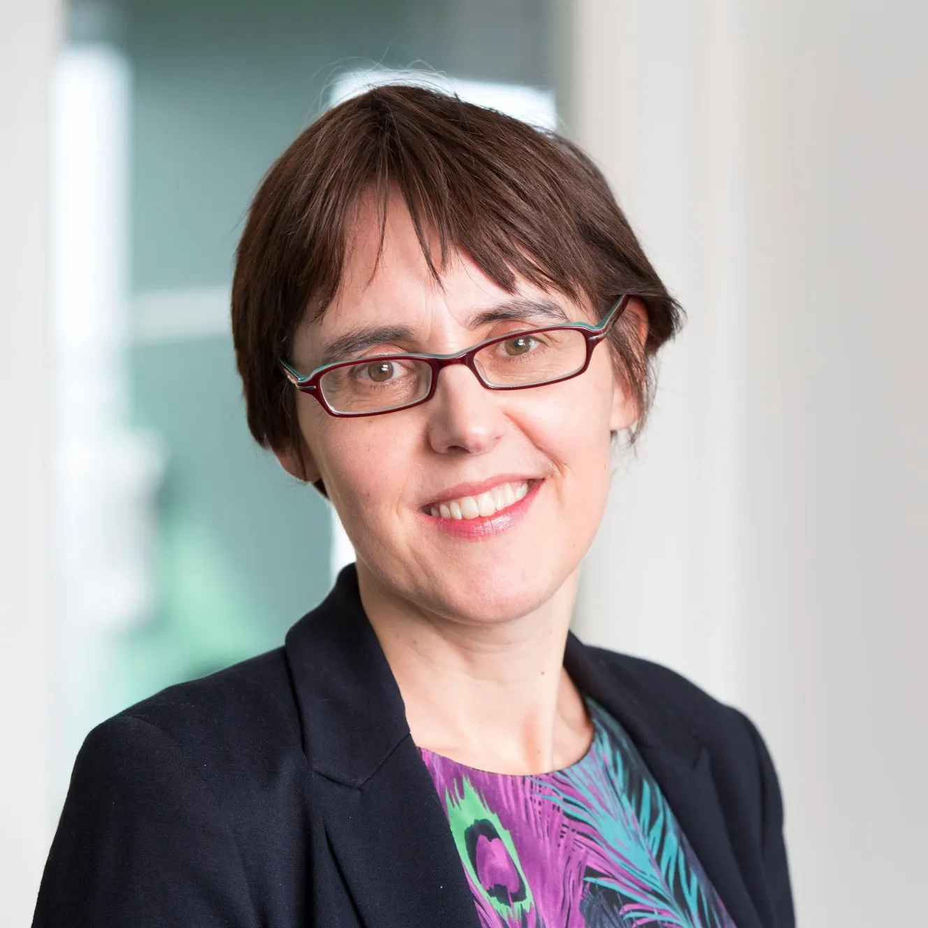 Headshot of Juliet Bouverie, CEO of the Stroke Association, smiling and wearing glasses with a dark jacket over a colorful top.