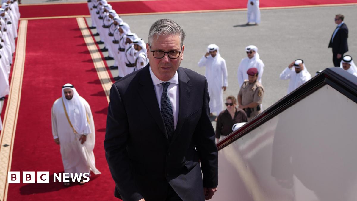 Keir Starmer boarding a plane at the airport in Doha, Qatar. There is a red carpet, lined with men, leading up to the plane