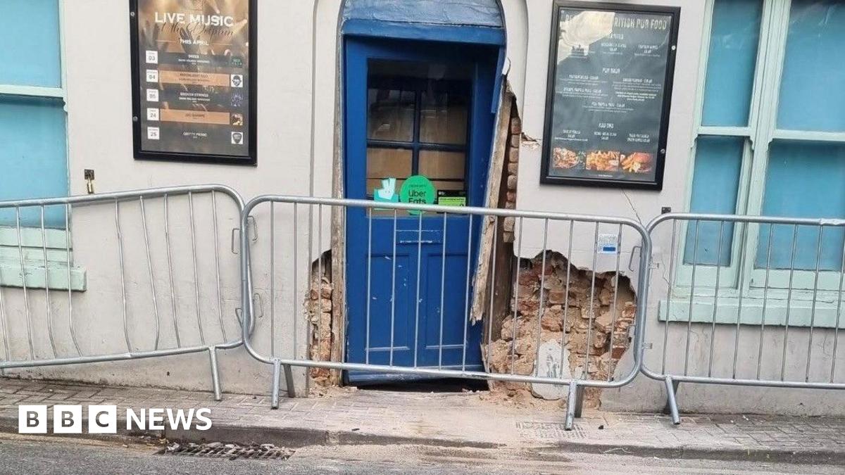 The entrance to the pub fenced off, with the wall and door damaged.