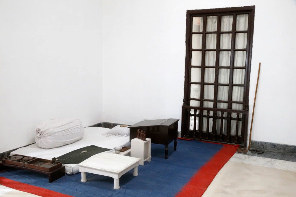 Simple room with a low bed, pillows, small tables, and wooden door. Suitable for meditation or quiet retreat