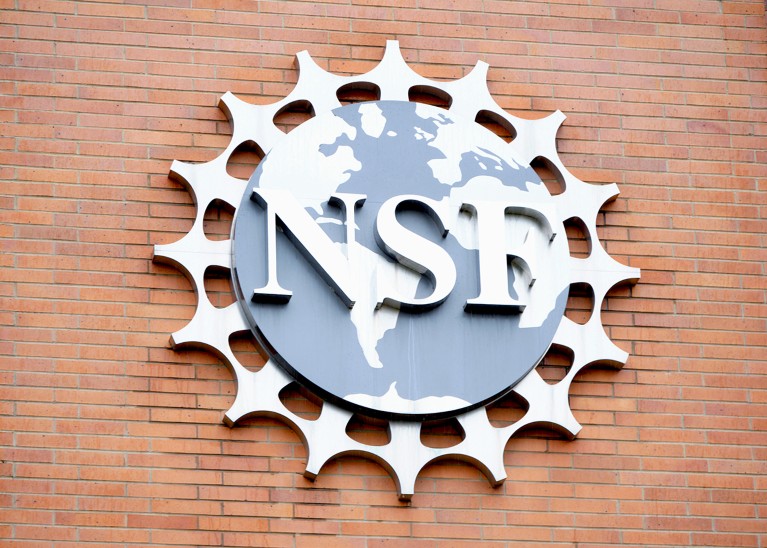 The NSF logo of the world map over a round gear shape on a brick building.