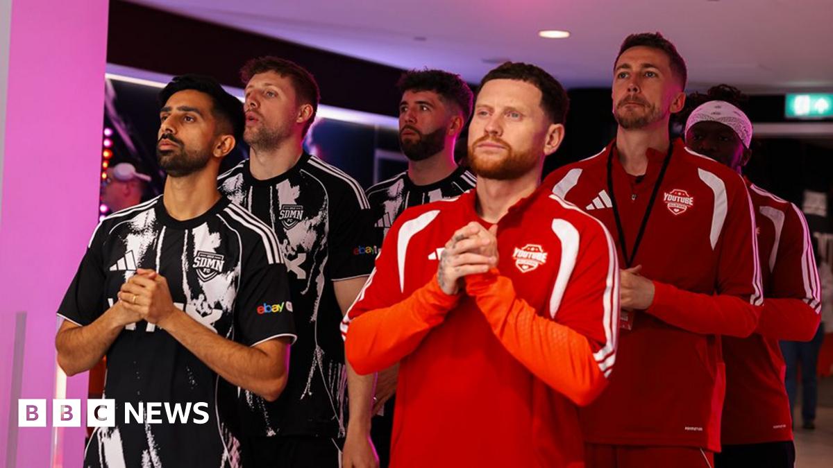 Three members from the Sidemen on the left dressed in a black jersey and three from the YouTubers Allstars dressed in red, standing in the tunnel with their hands together.