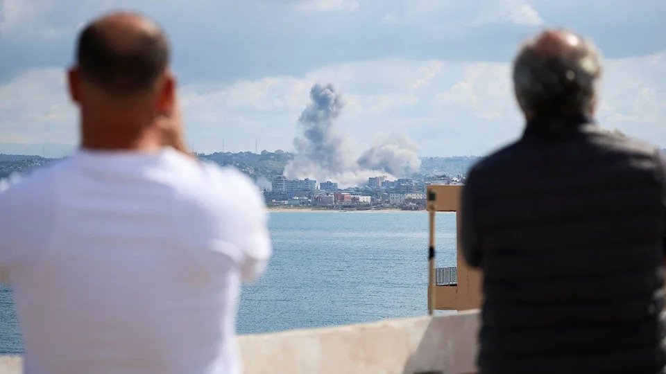 Two people with their backs to the camera look out over the Tyre skyline as a plume of smoke rises over the city on Wednesday.