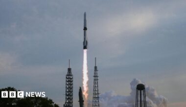 Blue Origin's New Glenn rocket taking off from a Florida launchpad with a hazy blue sky behind it.