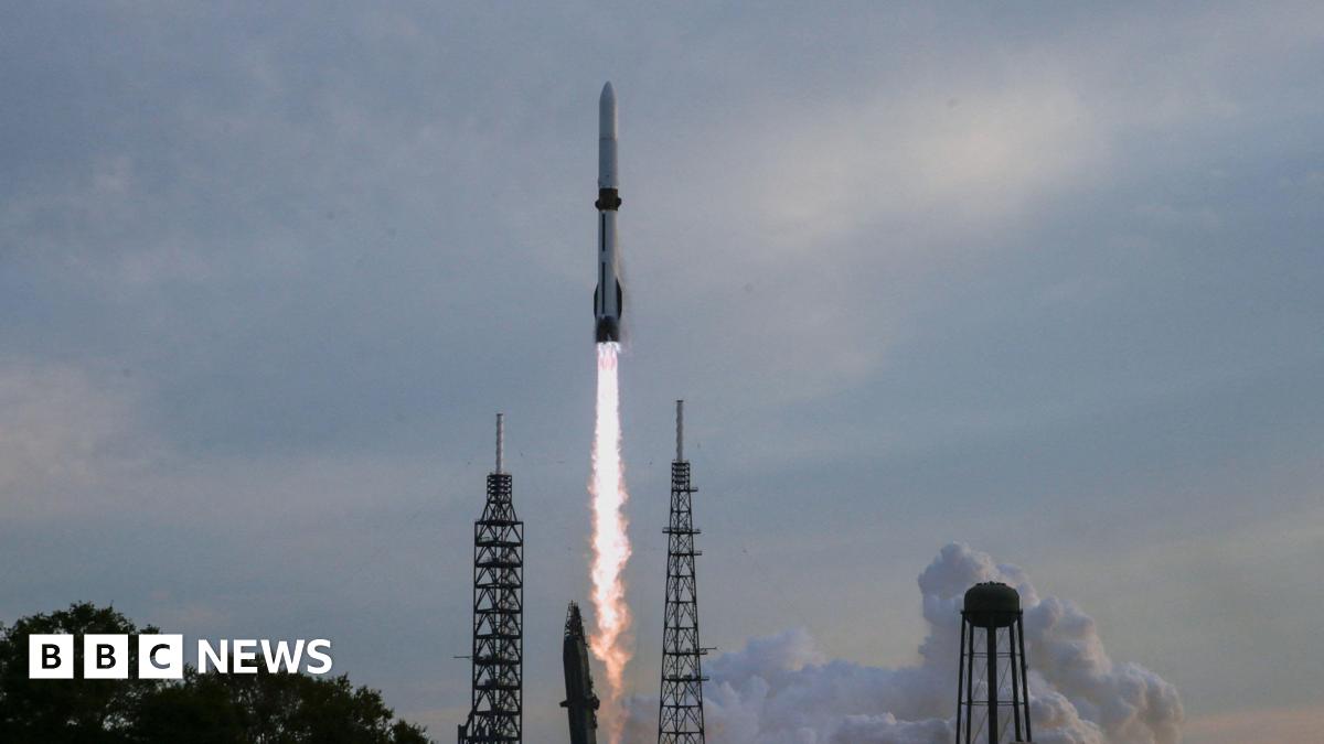 Blue Origin's New Glenn rocket taking off from a Florida launchpad with a hazy blue sky behind it.