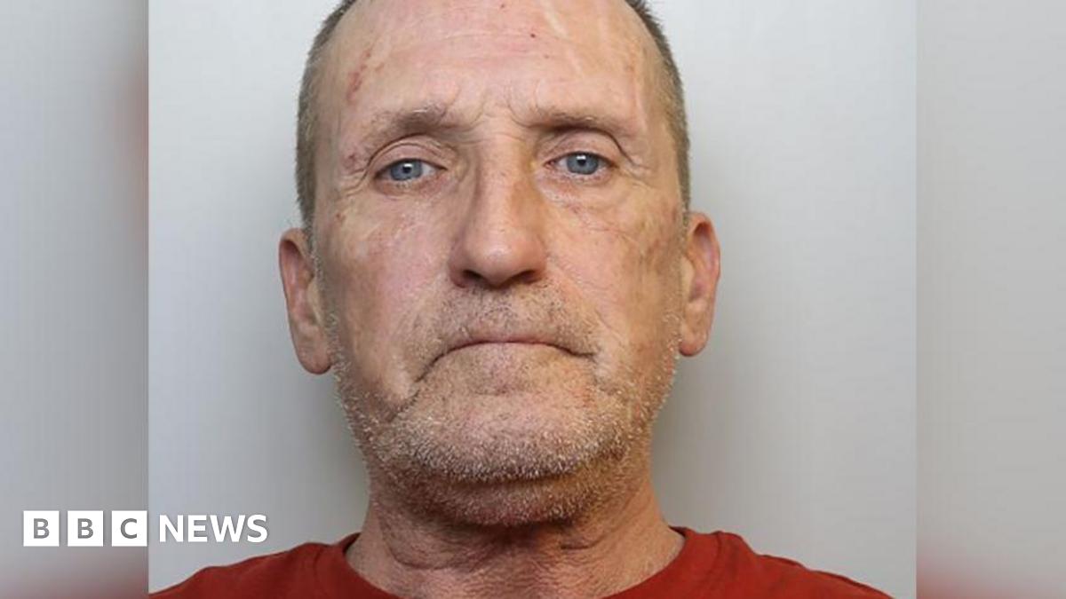 Stephen looks at the camera with a blank expression. He has short grey hair, a stubbly beard, and wears a red t-shirt.