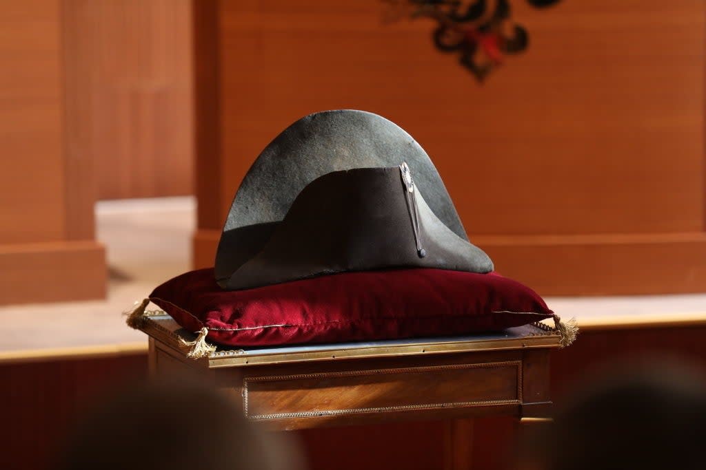 A historical bicorne hat displayed on a red velvet cushion atop a wooden table in a formal setting