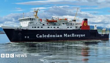 A black and white ship with red funnels. Caledonian MacBrayne is written on the side. There are blue skies and clouds in the background
