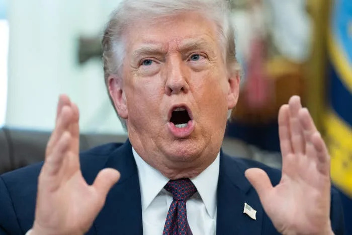 A person in a suit gestures while speaking, with an expressive face. Office-setting background