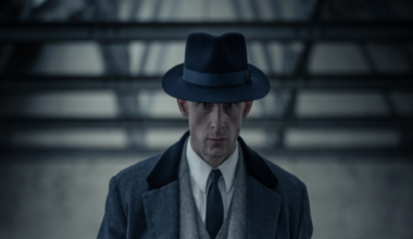 A Man in a 1950s suit walking with a serious expression on his face.