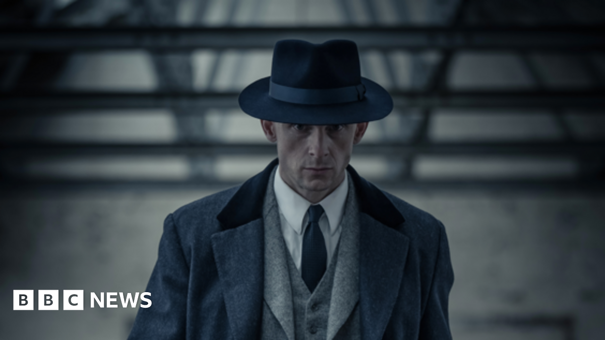 A Man in a 1950s suit walking with a serious expression on his face.