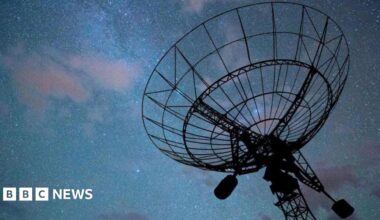 A radar disc pointed a dark night sky with an array of stars and clouds, tinged in purple, visible. The radar itself is in silhouette.