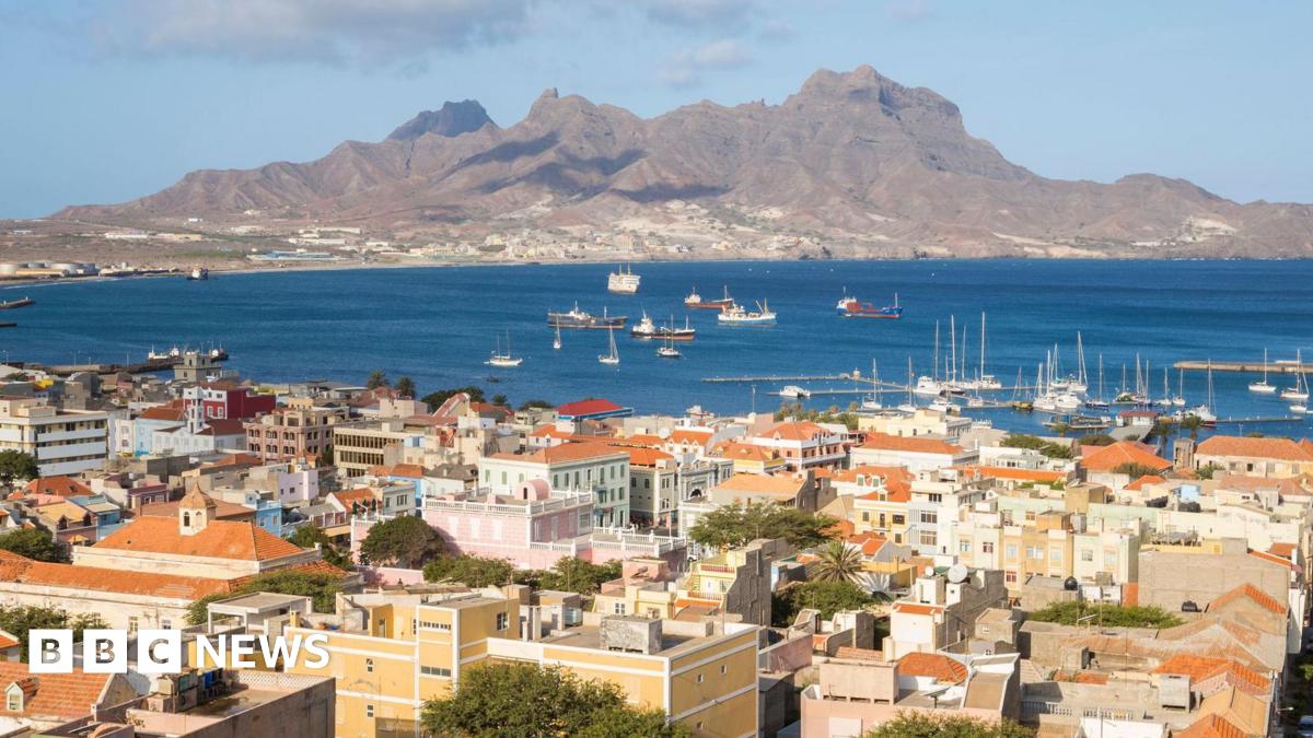 Elena Walsh, a 64-year-old woman with short ginger hair and wearing a red shirt, smiles with her arms around her husband, a main with grey hair and a blue shirt, and her son, a younger man with short brown hair, a beard and a grey jumper.