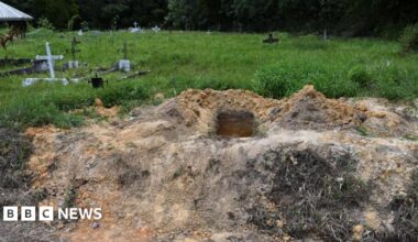 An open grave at the site in Cumuto, the rest of which shows graves with crosses on overgrown grass