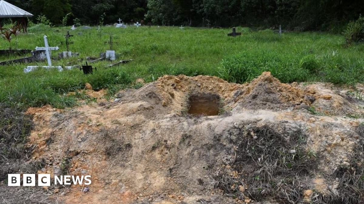 An open grave at the site in Cumuto, the rest of which shows graves with crosses on overgrown grass