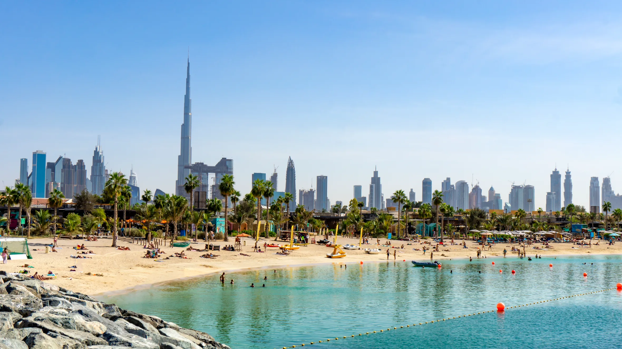People relaxing on a beach in Dubai with the city skyline and the Burj Khalifa in the background.