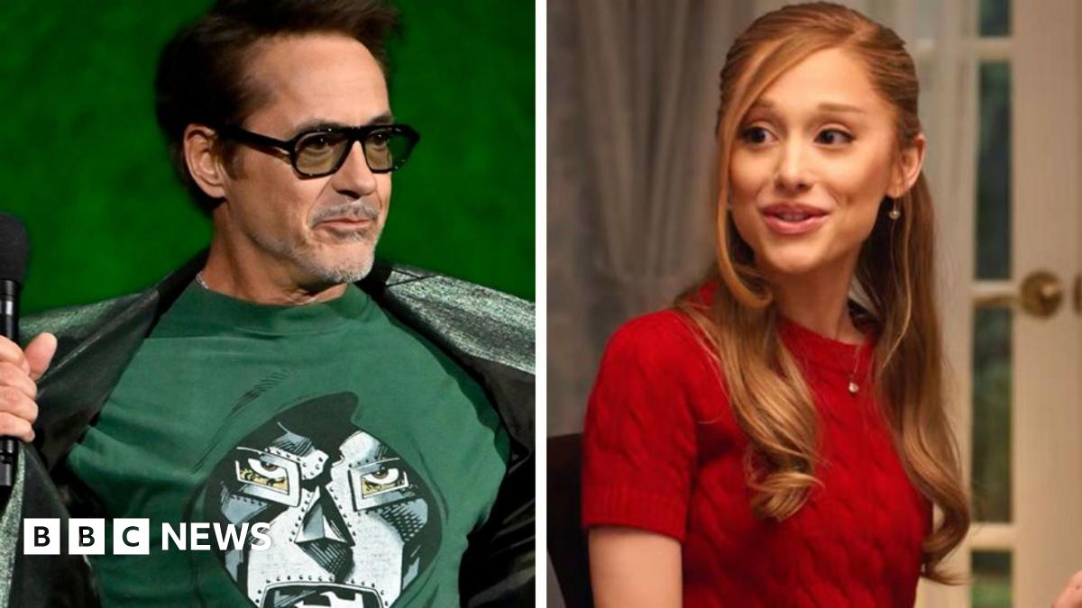 Robert Downey Jr on stage at CinemaCon, opening his jacket to reveal a T-shirt showing the masked face of his character Doctor Doom