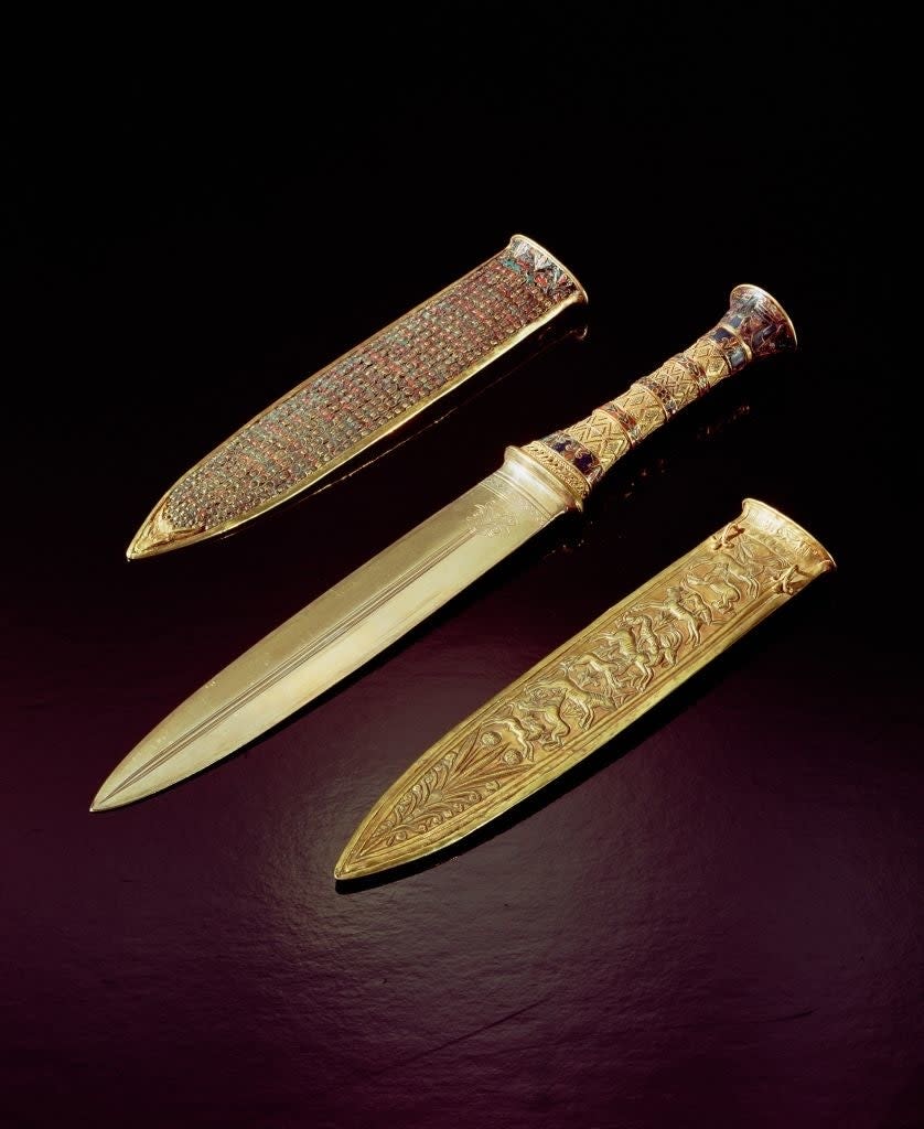 An ancient ornate dagger with a decorated handle and sheath displayed on a dark surface