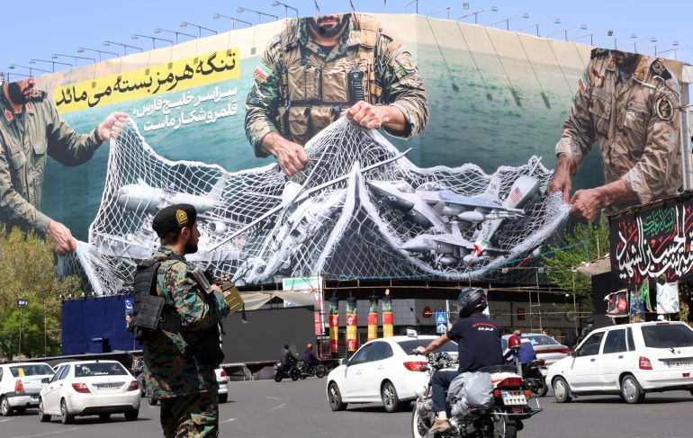 epa12870206 A member of the Iranian security forces watches over traffic passing a huge political billboard reading in Persian ’The Strait of Hormuz will remain closed', in Enghelb square in Tehran, Iran, 05 April 2026. Iran's Revolutionary Guards (IRGC) said a US aircraft that had been searching for the crew member of a missing US fighter jet had been destroyed, Iranian media reported on 05 April 2026. EPA/ABEDIN TAHERKENAREH