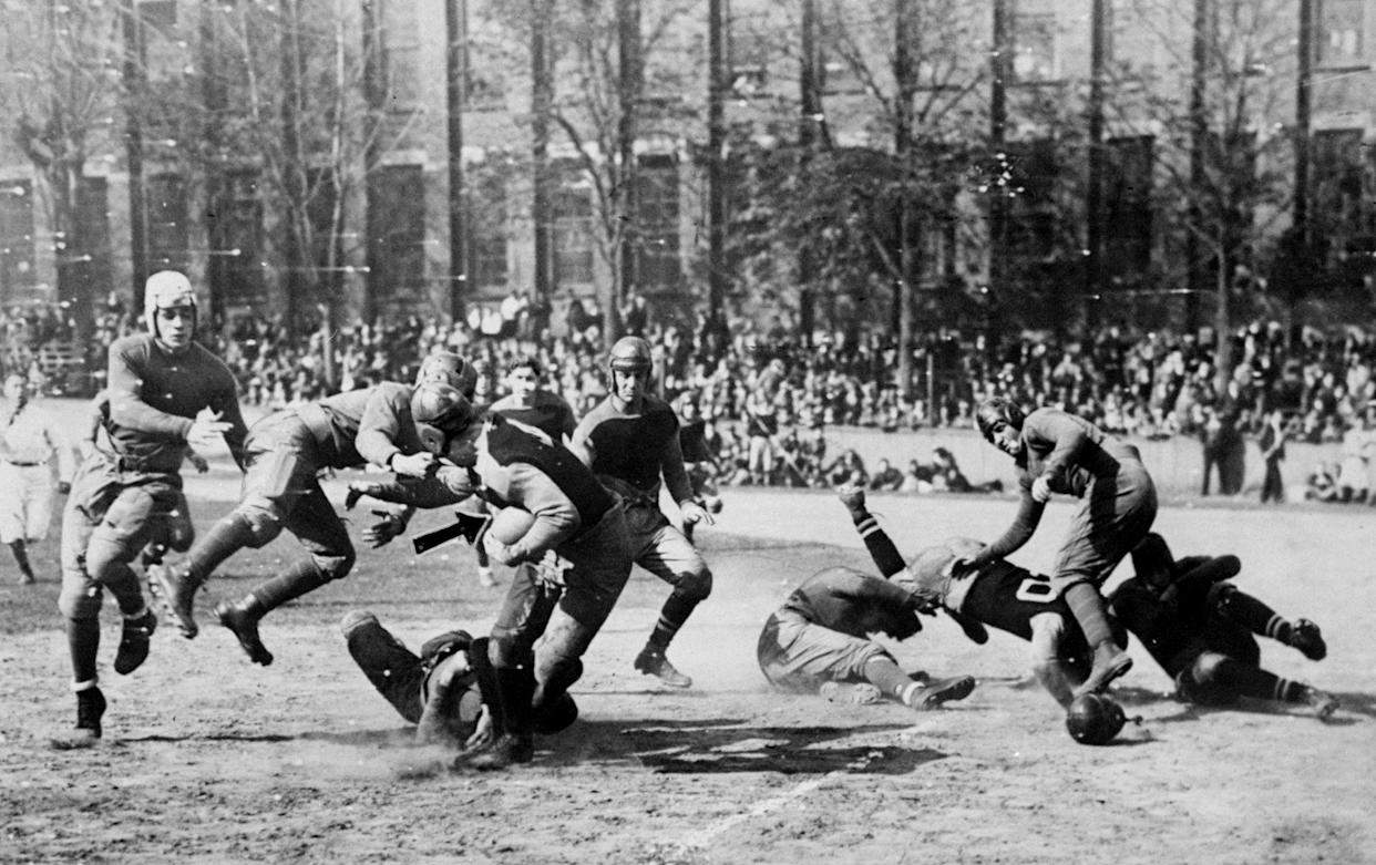 Players in leather helmets tackle a running back circa 1920