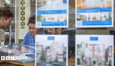Couple looking at paperwork in an estate agent with pictures of homes for sale in the foreground.