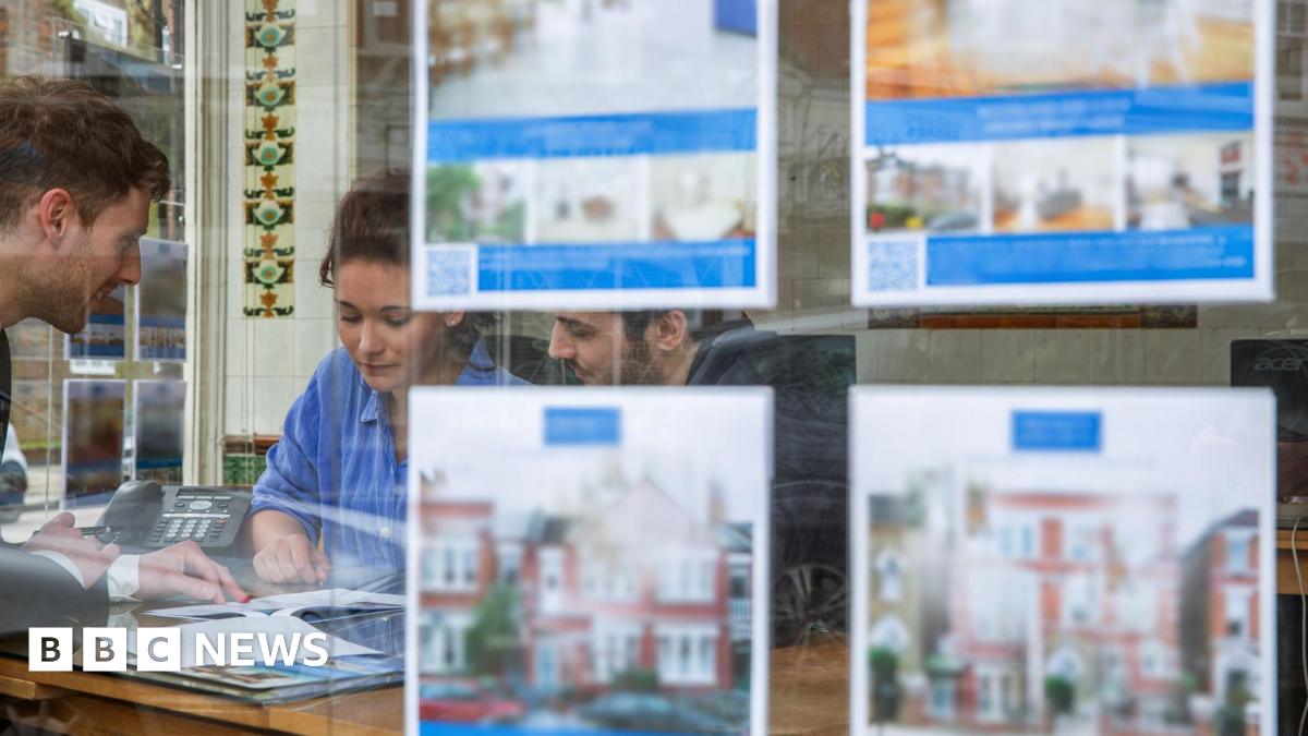Couple looking at paperwork in an estate agent with pictures of homes for sale in the foreground.
