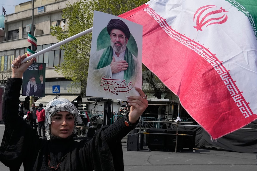 A young woman holding a picture of the ayatollah and an Iranian flag.