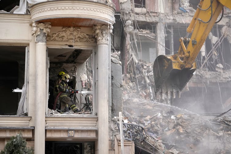 A bulldozer in front of an ornate, heavily damaged apartment building.