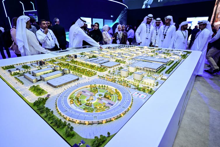 men wearingwhite robes and headdresses stand over a model of an industrial park
