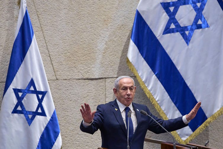 Benjamin Netanyahu in the Knesset flanked by Israeli flags.: