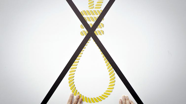 A person holds a large placard of a noose  with a big cross through it.