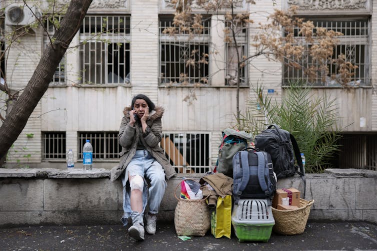 A weeping woman on her phone sitting next to her personal belongings.