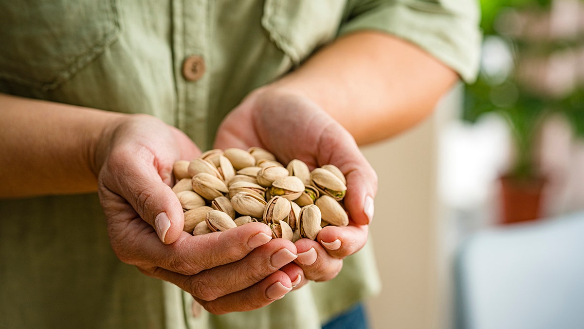 Hands holding a pile of pistachio nuts.