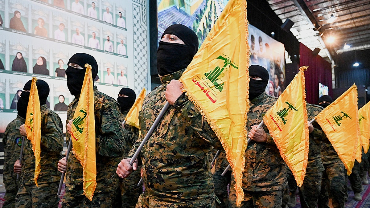 Fadel Itani standing in front of Hezbollah flags and banners