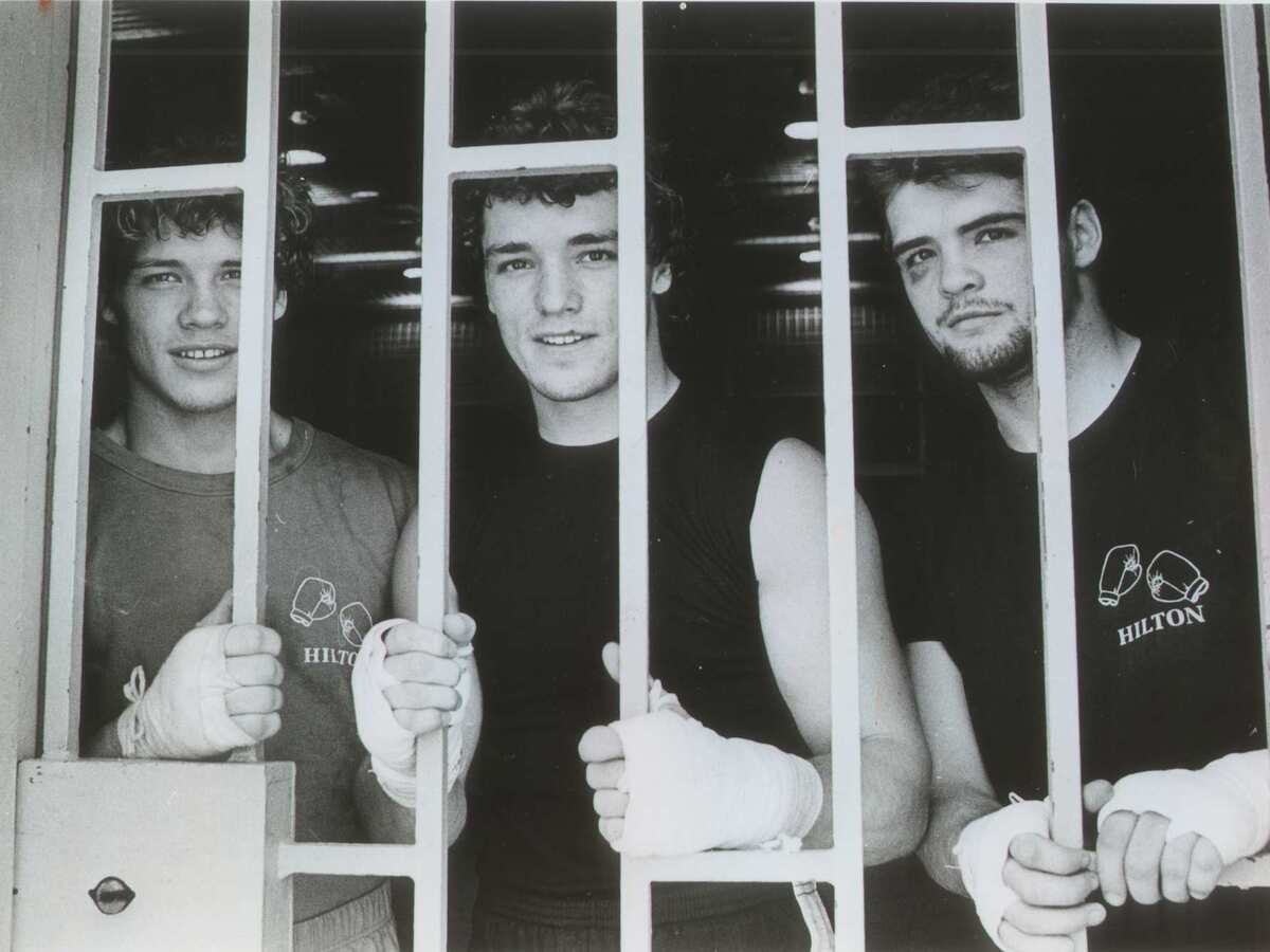 Three young men pose for a photo behind prison bars.