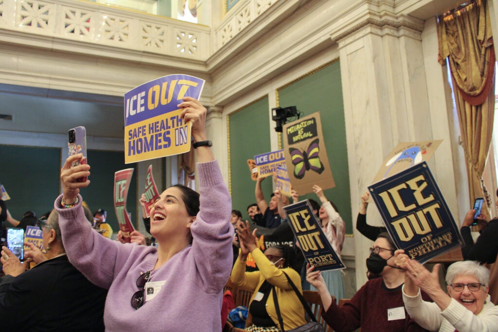 Activists hold up signs in council chambers that say 'ICE Out'