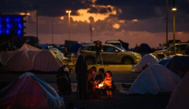 Displaced people warm up around a fire outside their tent along Beirut