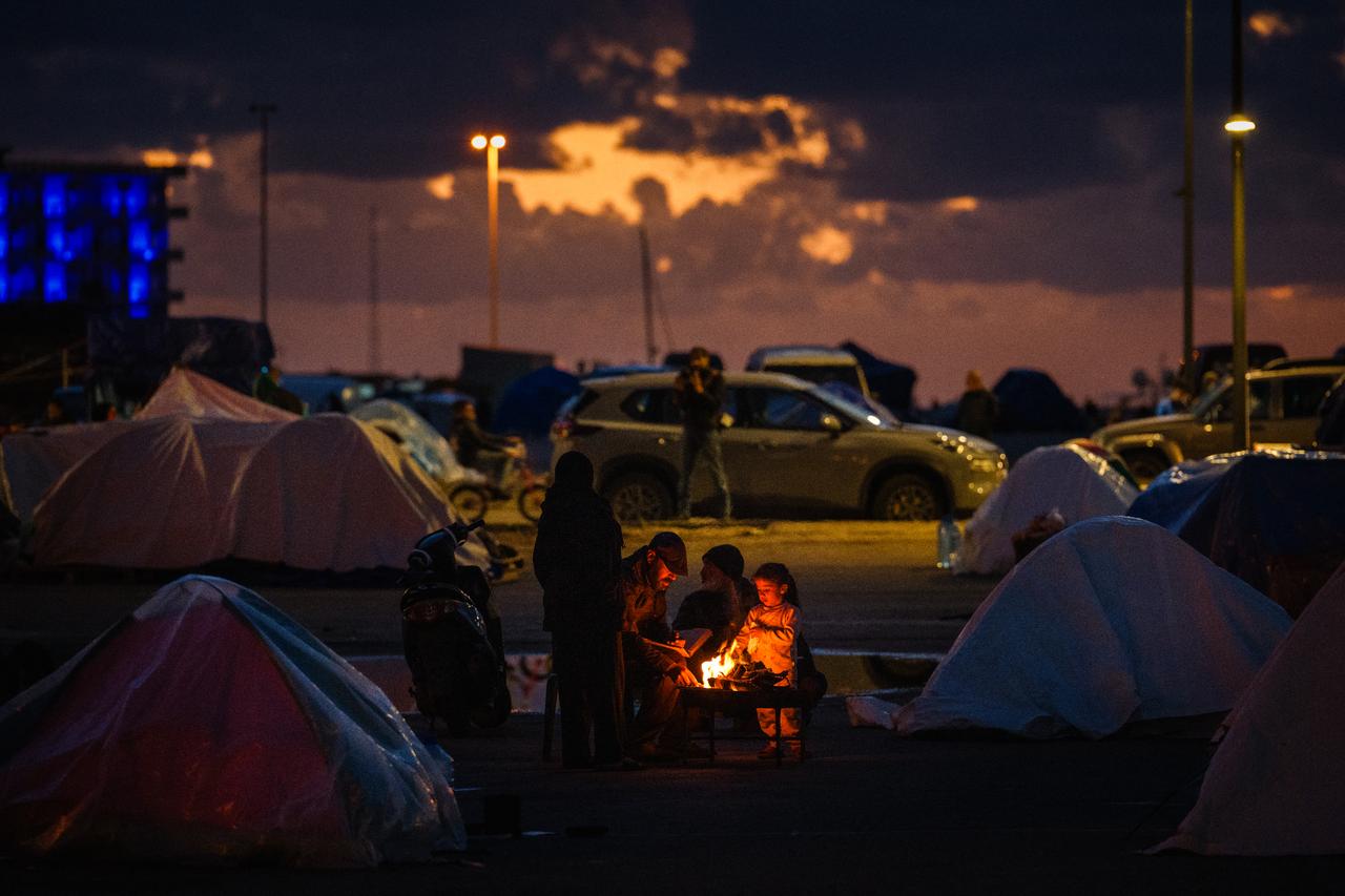 Displaced people warm up around a fire outside their tent along Beirut