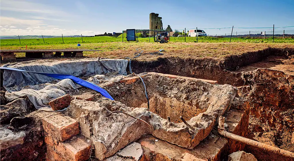 Ancient ruins excavation with exposed stone structures and archaeological tools.