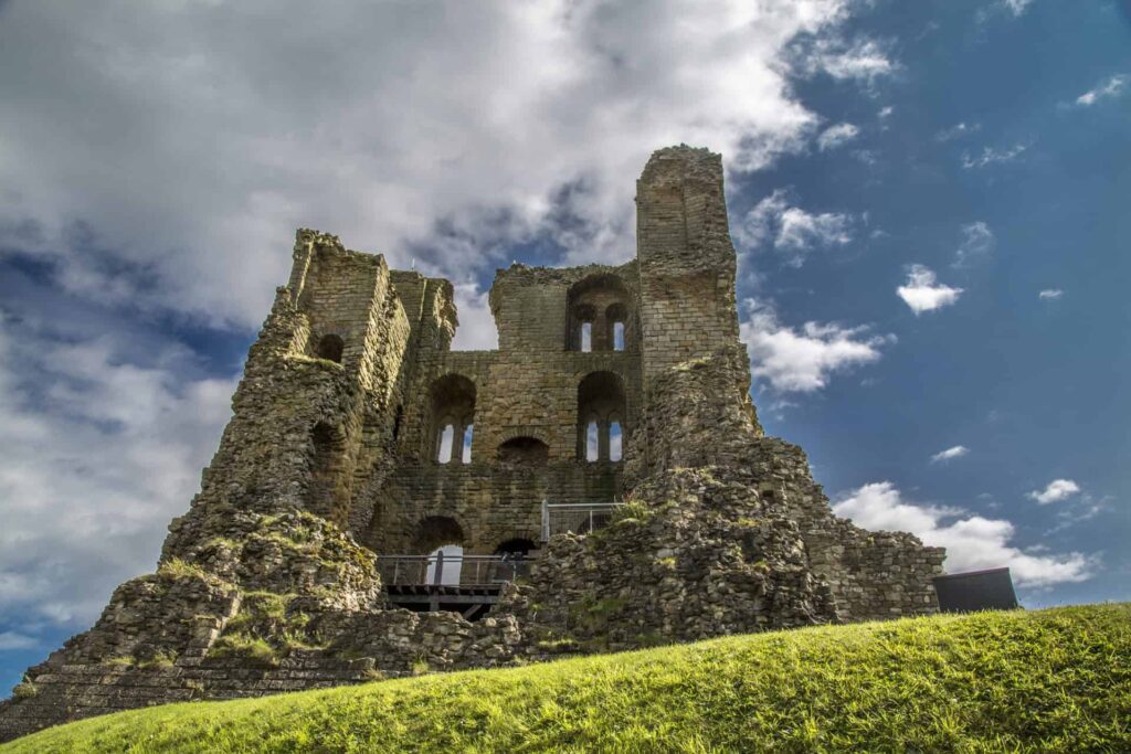 Ancient castle ruins with stone walls and arched windows under a cloudy sky.